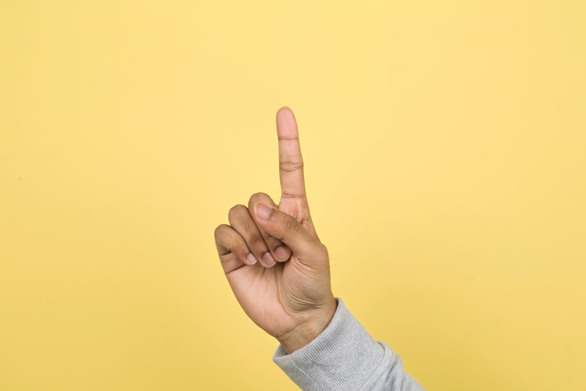 hand in fist with pointer finger pointing up against a yellow background