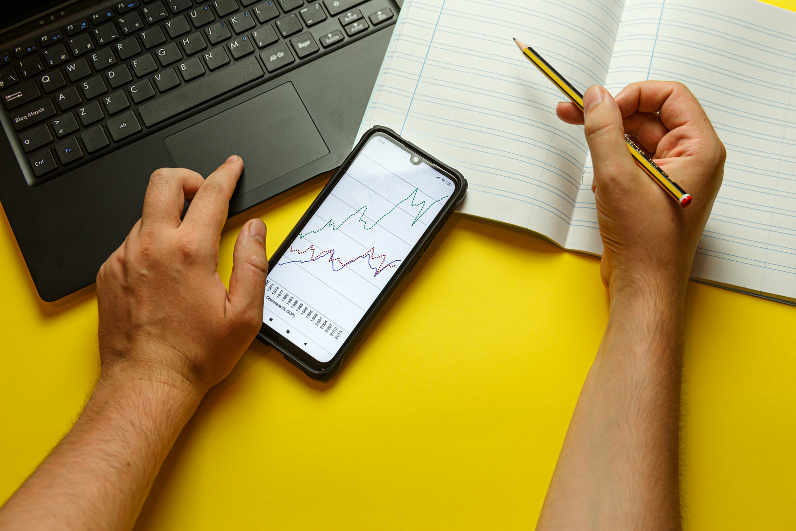 multitasking with a laptop, phone and notebook with hands writing using a pencil
