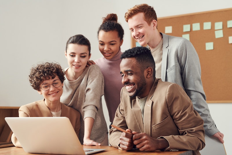 group of business casual people smiling while look at one laptop screen